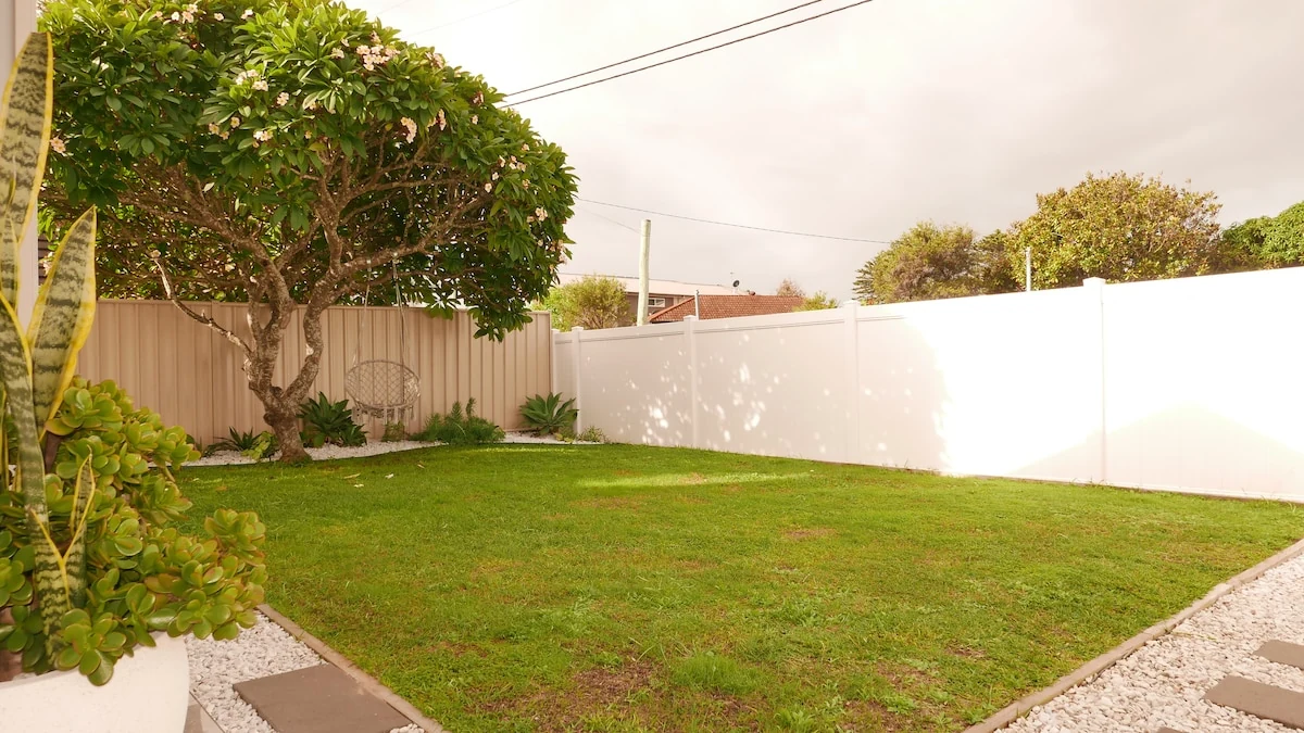 Fully fenced grass backyard with swing under the tree